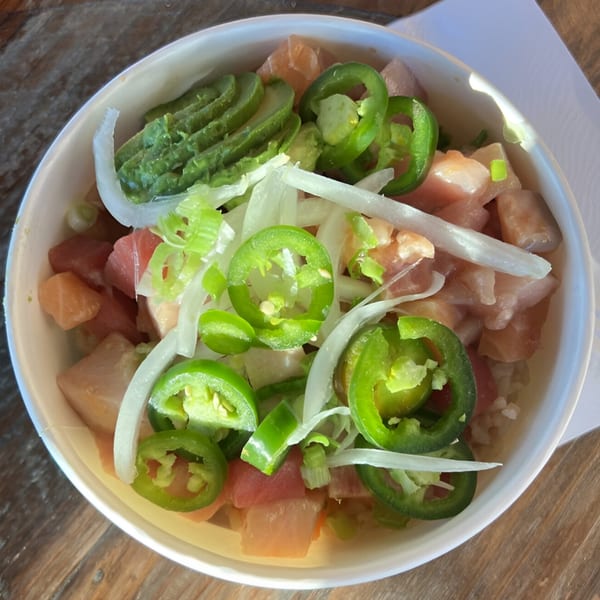 Poke Chop poke bowl with tuna, avocado, jalapenos, and onions on a wooden table.