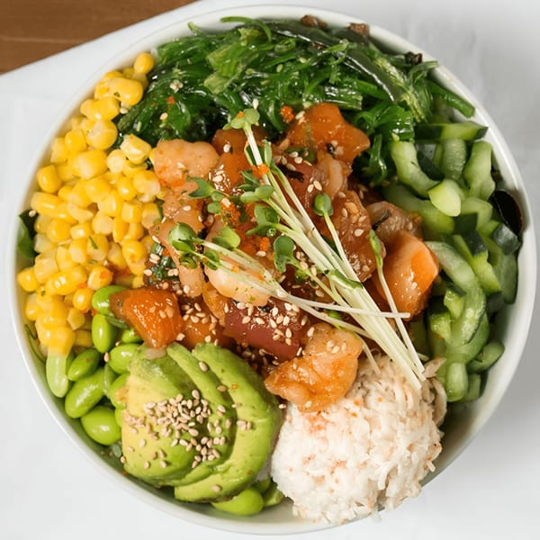 A vibrant Poke Chop poke bowl filled with tuna, salmon, corn, seaweed, cucumber, avocado, and edamame.